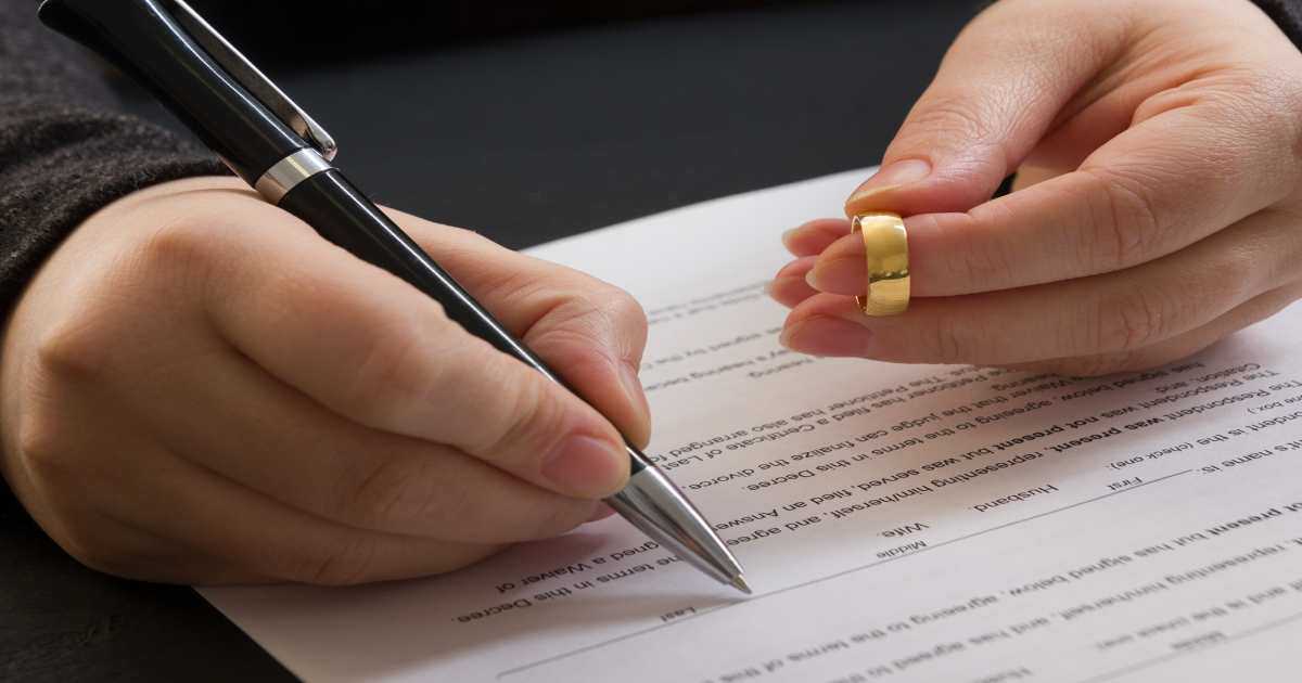 Person Holding Wedding Ring While Signing Divorce Papers